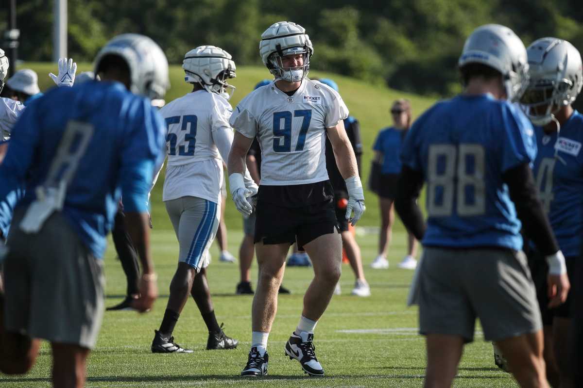 Aidan Hutchinson stands at training camp as players walk around him